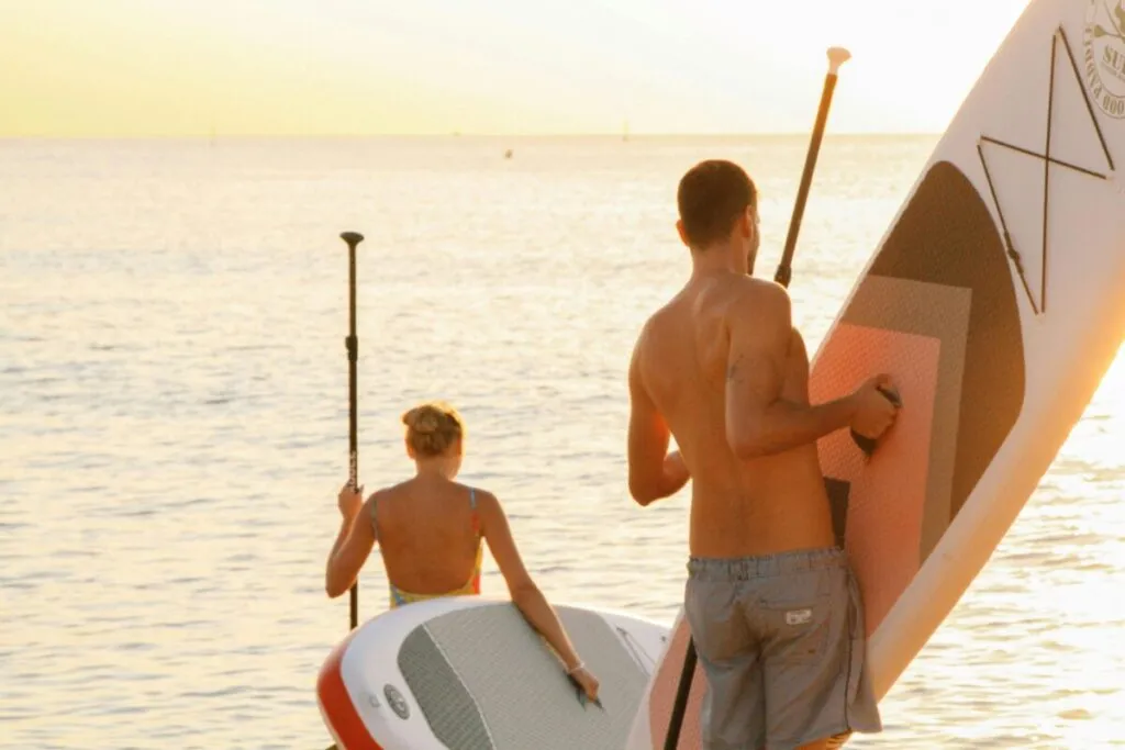 Personas practicando paddleboarding en San Diego durante el atardecer, con vistas del skyline y aguas tranquilas