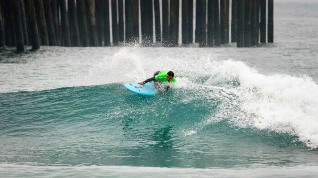 Martín Díaz compite en el mar de Oceanside con la bandera mexicana ondeando al fondo.