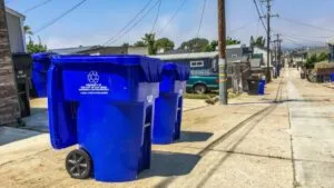 Camión de recolección de basura en zona residencial costera de San Diego con contenedores alineados en la banqueta y cielo nublado que refleja las nuevas tarifas en el recibo predial