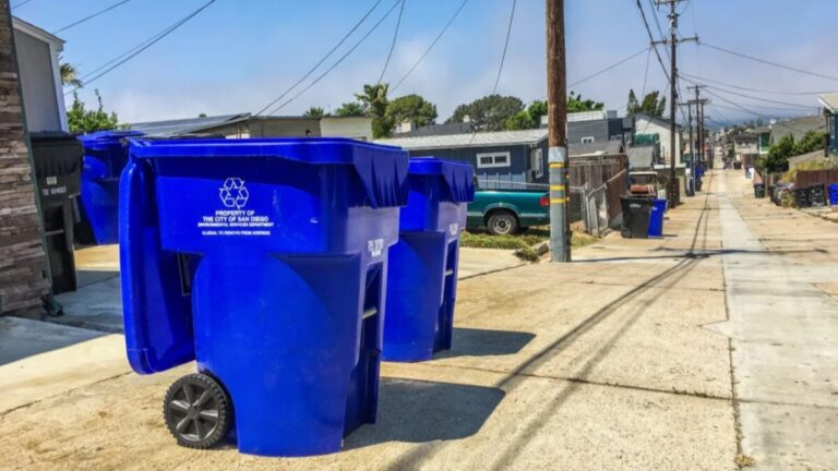 Camión de recolección de basura en zona residencial costera de San Diego con contenedores alineados en la banqueta y cielo nublado que refleja las nuevas tarifas en el recibo predial