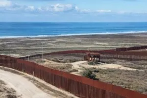 Fotografía editorial de muro fronterizo en San Diego con ambulancia y personal médico atendiendo a migrantes heridos