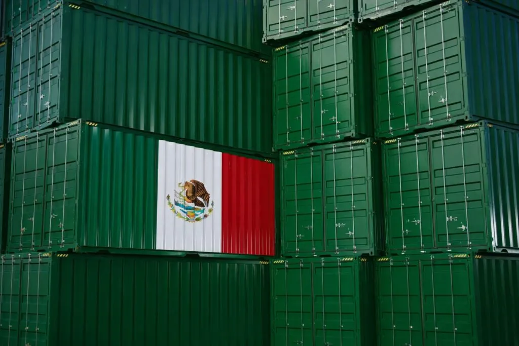 Contenedores verdes apilados, uno con la bandera de México, simbolizando crecimiento exportador