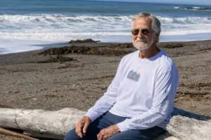 Michael Fickel sentado frente al mar en Pacific Grove, California, con vestimenta deportiva y expresión serena