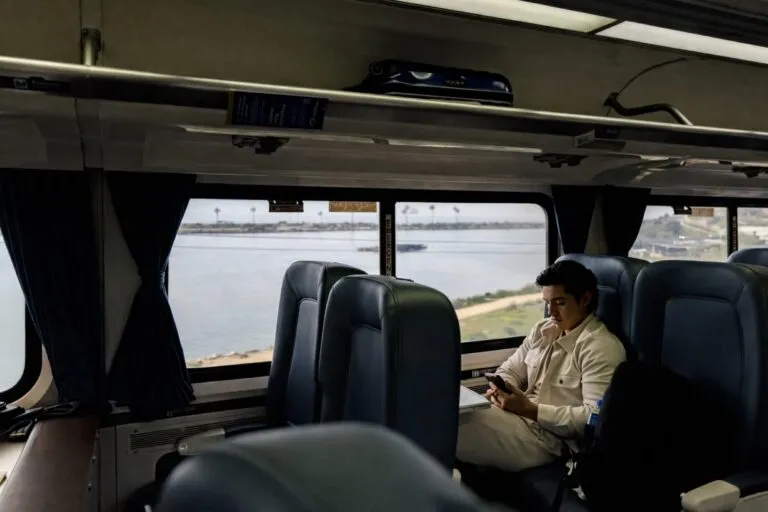 Persona viajando en el tren Pacific Surfliner, con vista al mar desde el interior del vagón en la ruta San Diego–Los Ángeles