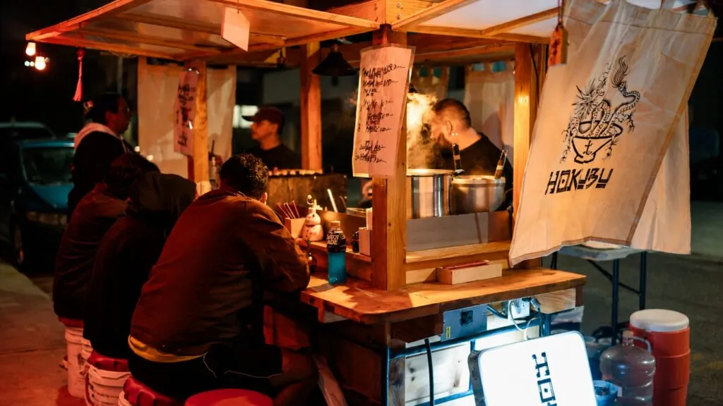 Hokubu ramen en Tijuana servido en carreta japonesa callejera con ambiente urbano nocturno y clientes disfrutando