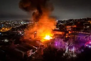 Incendio en vivienda en la colonia Postal de Tijuana con bomberos controlando las llamas y protegiendo casas cercanas.