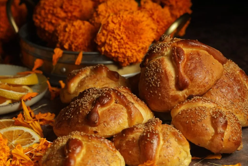 Pan de muerto tradicional mexicano cubierto de azúcar y decorado con figuras de huesos, acompañado de flores de cempasúchil.