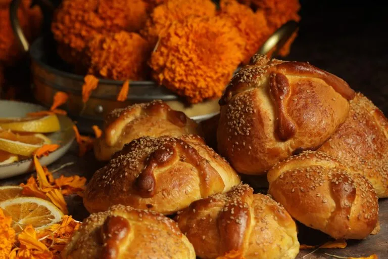 Pan de muerto tradicional mexicano cubierto de azúcar y decorado con figuras de huesos, acompañado de flores de cempasúchil.